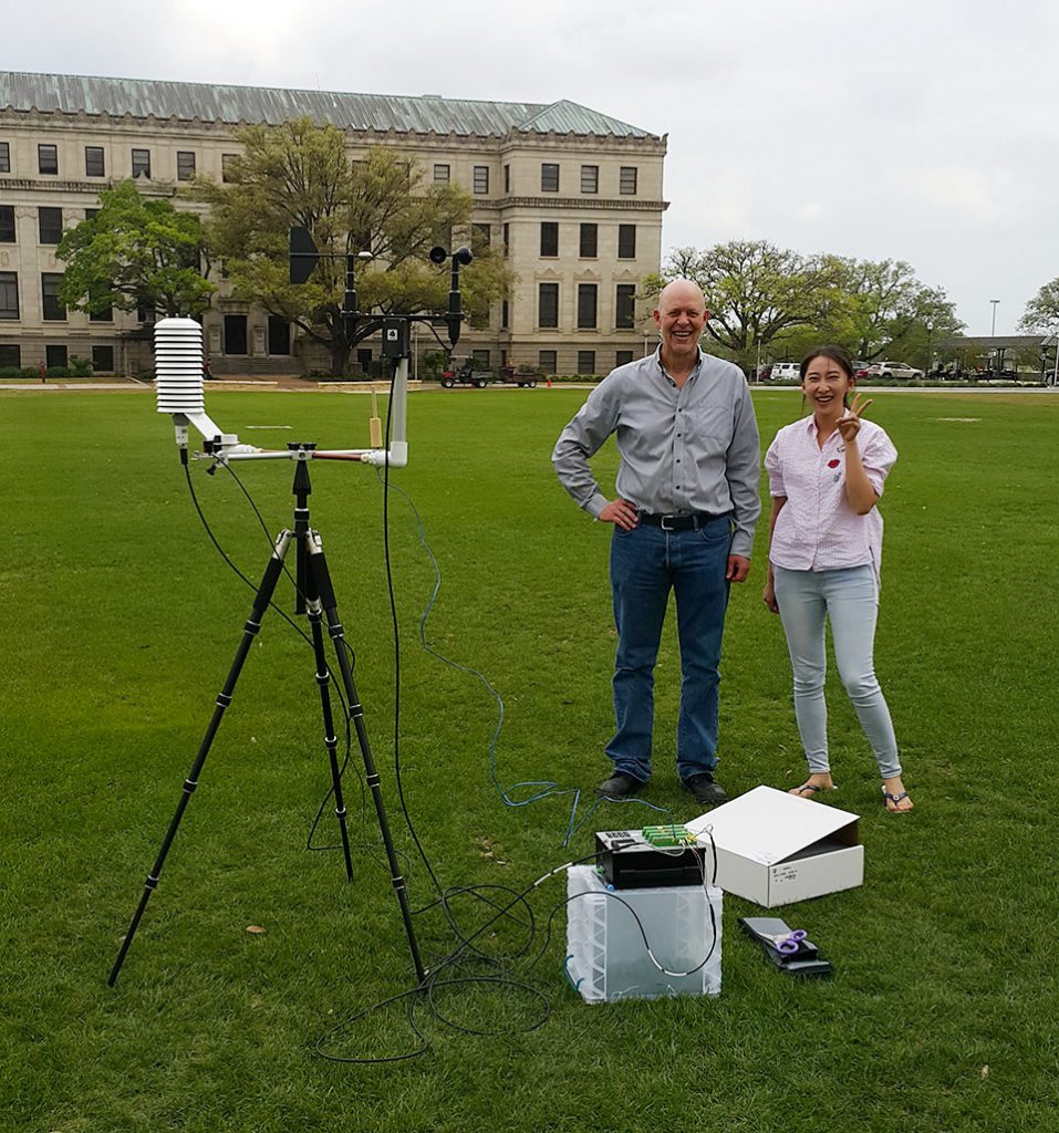 Two people stand next to technical equipment on a lawn.